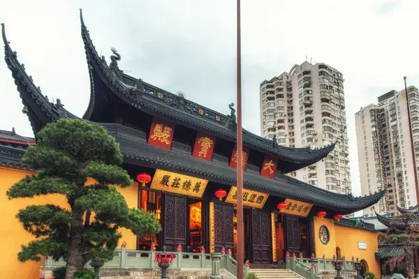 Fachada de um templo chinês com paredes amarelas e telhados pretos ornamentados, contrastando com prédios residenciais altos ao fundo.