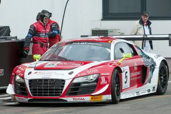 Carro de corrida Audi R8 LMS da categoria GT parado nos boxes durante evento de endurance, com equipe técnica ao redor, típico das 24 Horas de Le Mans e campeonatos de longa duração.
