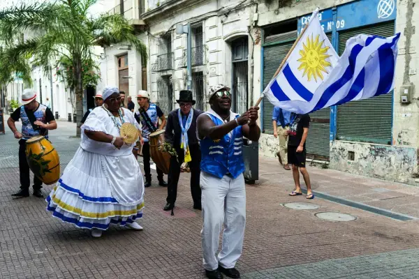 Apresentação de candombe nas ruas de Montevidéu, com músicos, dançarinos e bandeira do Uruguai.
