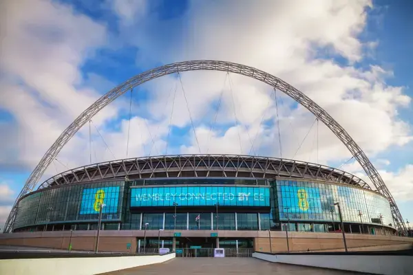 Vista externa do Wembley Stadium em Londres, com o arco metálico de 134 metros sobre a cobertura e fachada de vidro na entrada principal.