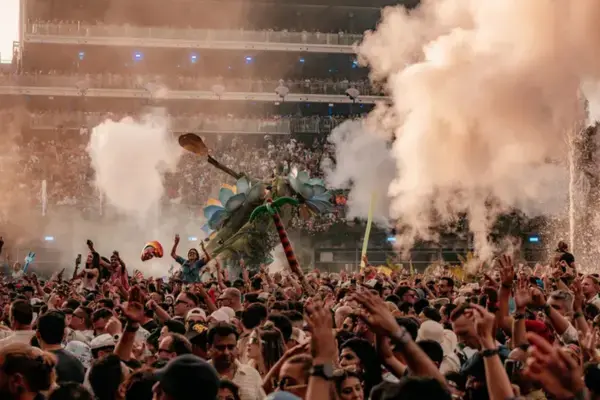 Multidão celebrando no Tomorrowland Bélgica com fumaça colorida e decoração temática ao fundo